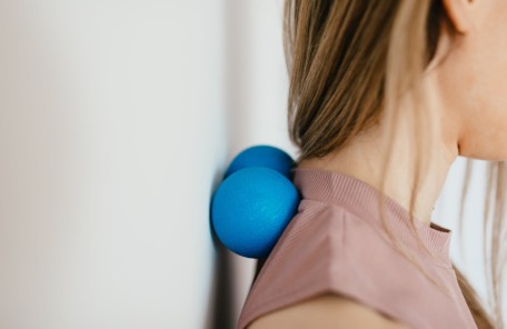 crop woman massaging neck with balls by leaning on wall